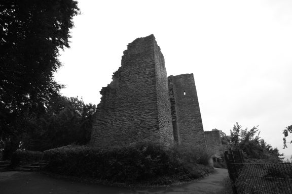 Ruinen einer alten Burg umgeben von Bäumen und Sträuchern, in Schwarz-Weiß.