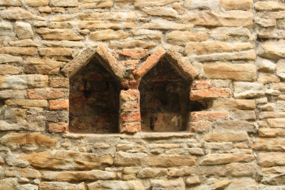 Zwei kleine Nischen in einer steinernen Wand mit roten Backsteinen.