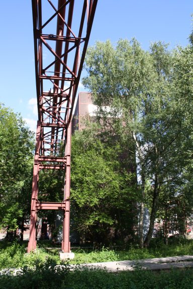 Eisenbahnbrücke mit rotem Stahlgestell, umgeben von Bäumen und Grünflächen.