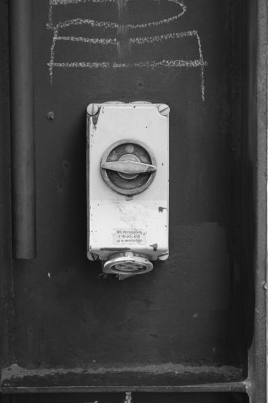 Ein alter, runder Türöffner aus Metall an einer schwarzen Wand.