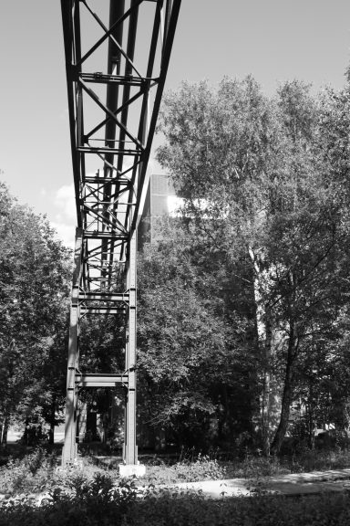 Eisenbahnbrücke mit Stahlträgern, umgeben von grünen Bäumen und urbaner Umgebung.