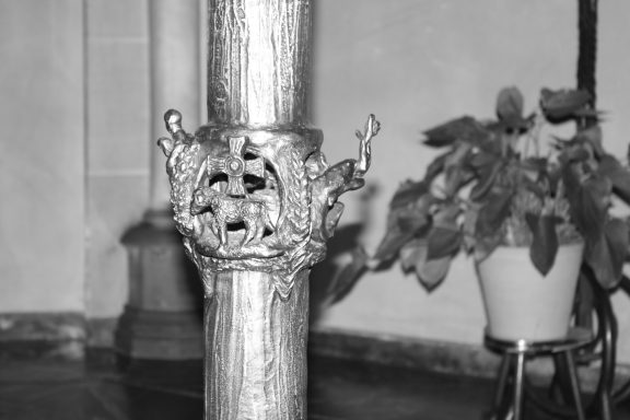 Ornamentierte Säule mit Pflanzen im Hintergrund, schwarz-weiß.