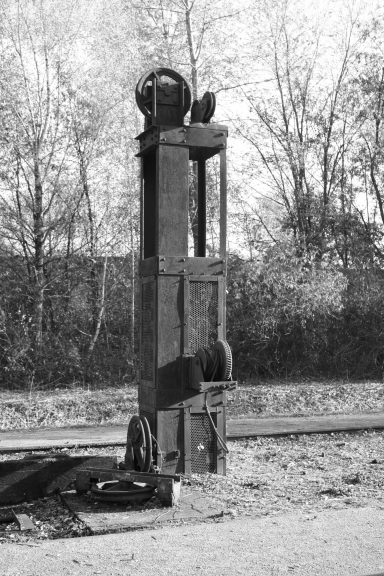 Ein alter Bahnsignalpost in Schwarz-Weiß, umgeben von Bäumen.