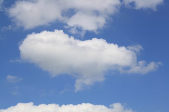 Wolkiger Himmel mit hellen, flauschigen Wolken vor blauem Hintergrund.