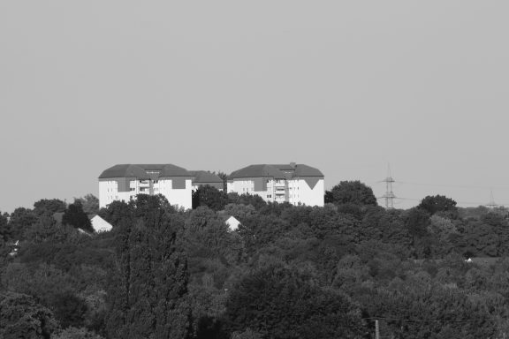 Zwei weiße Gebäude auf einem Hügel, umgeben von Bäumen und Vegetation.