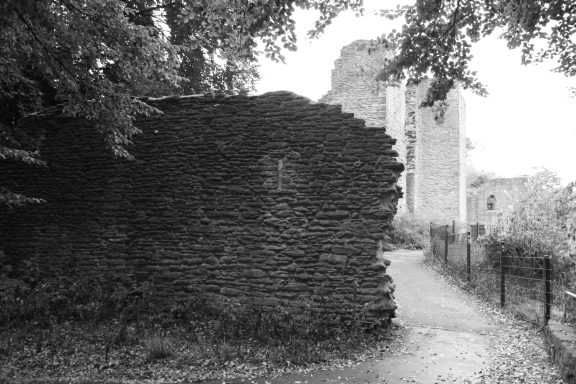 Ruine einer Mauer mit Blick auf ein historisches Gebäude hinter Bäumen.